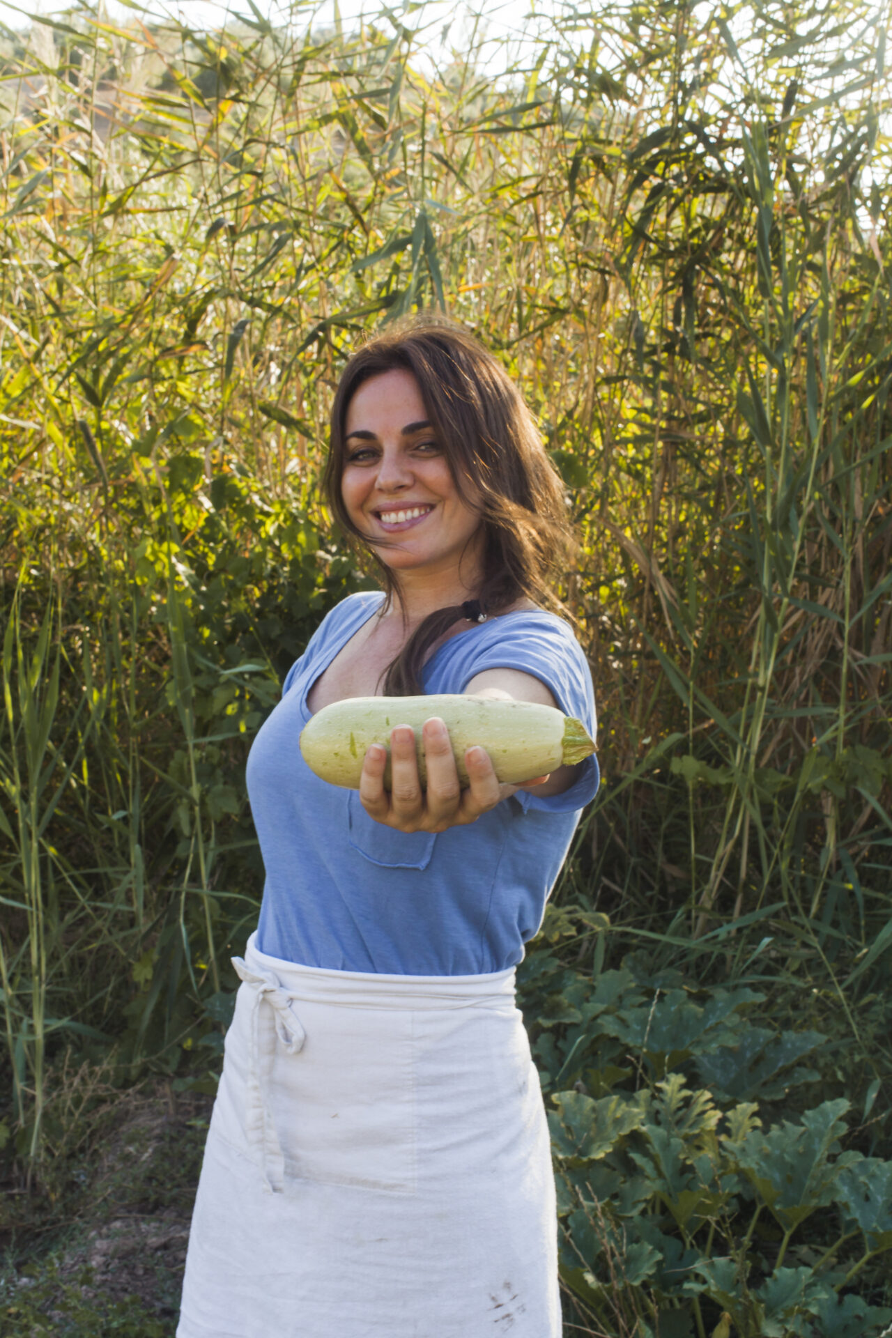 mujer-sonriente-de-pie-en-el-campo-mostrando-calabaza-cosechada